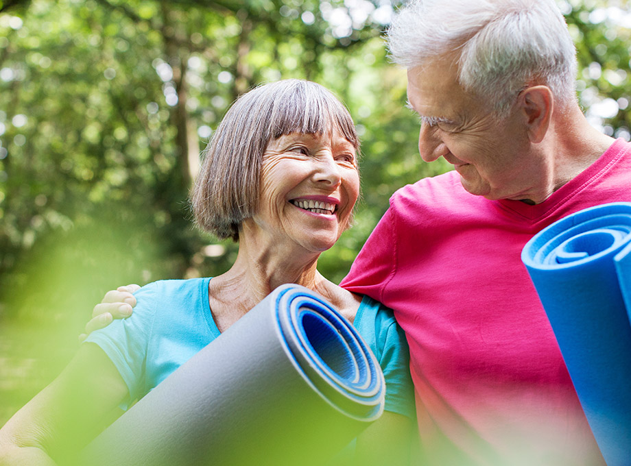 A senior man and a senior woman hold rolled up exercise mats