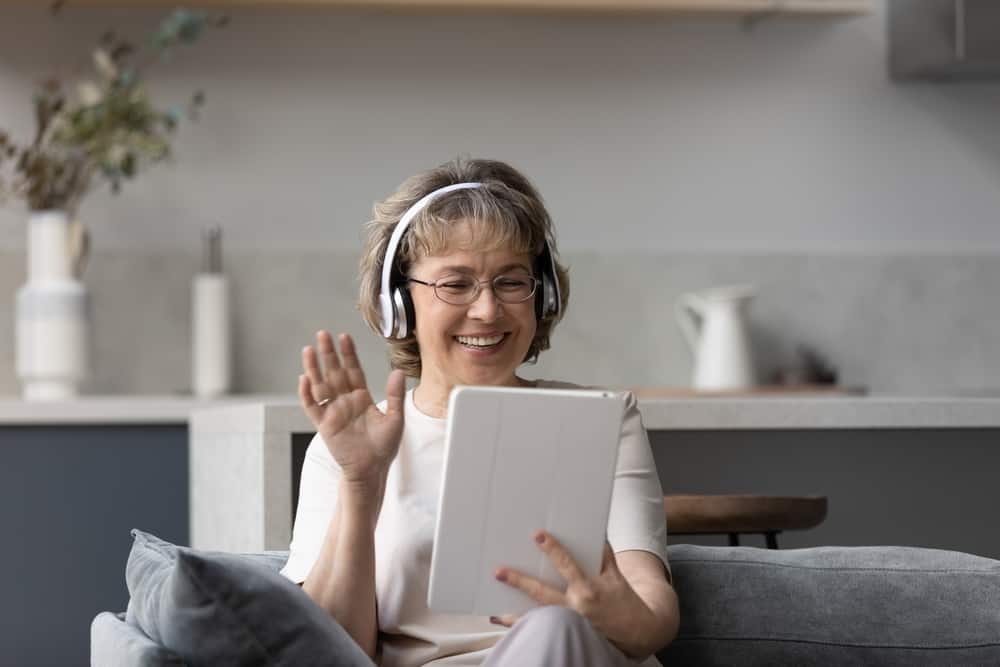 A senior woman wearing wireless headphones and using a tablet to video call someone
