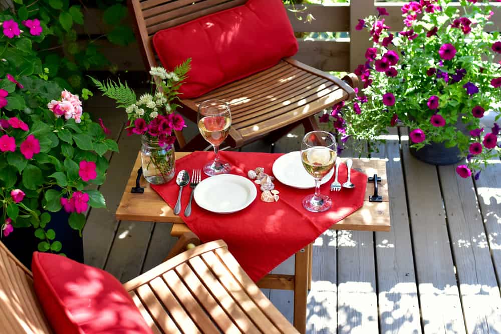 A patio with deck furniture with red cushions and blooming flowers