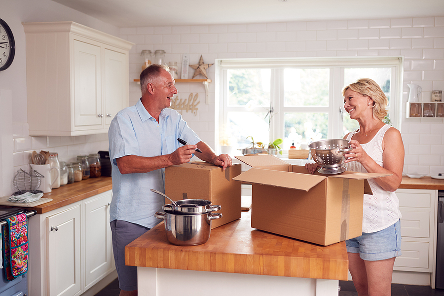 Image Alt Text: A senior couple smiles while unpacking moving boxes.