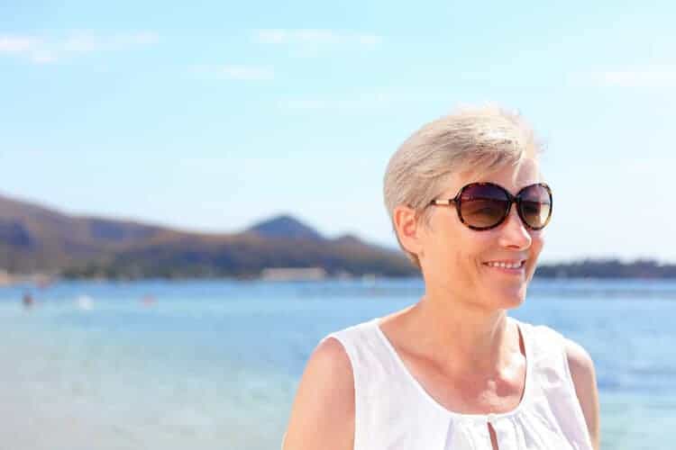Senior woman at the beach practicing proper eye care by wearing sunglasses.