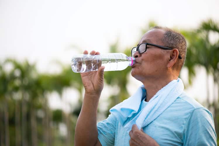 A senior man drinking water to prevent dehydration in the summer.