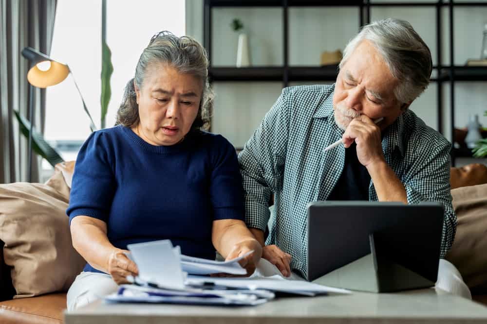 a senior man and a senior woman looking confused at paperwork on a desk