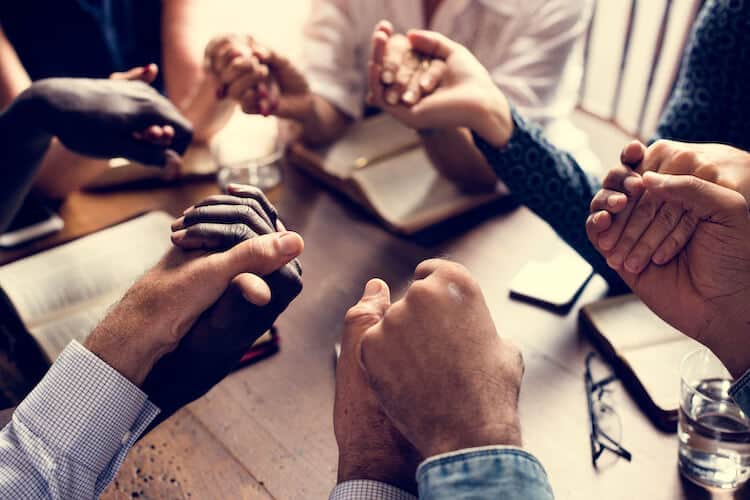 Group of seniors holding hands in prayer.
