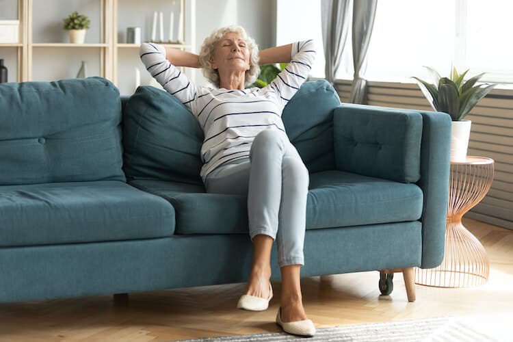 A senior woman on a couch using stress relief tips to relax.