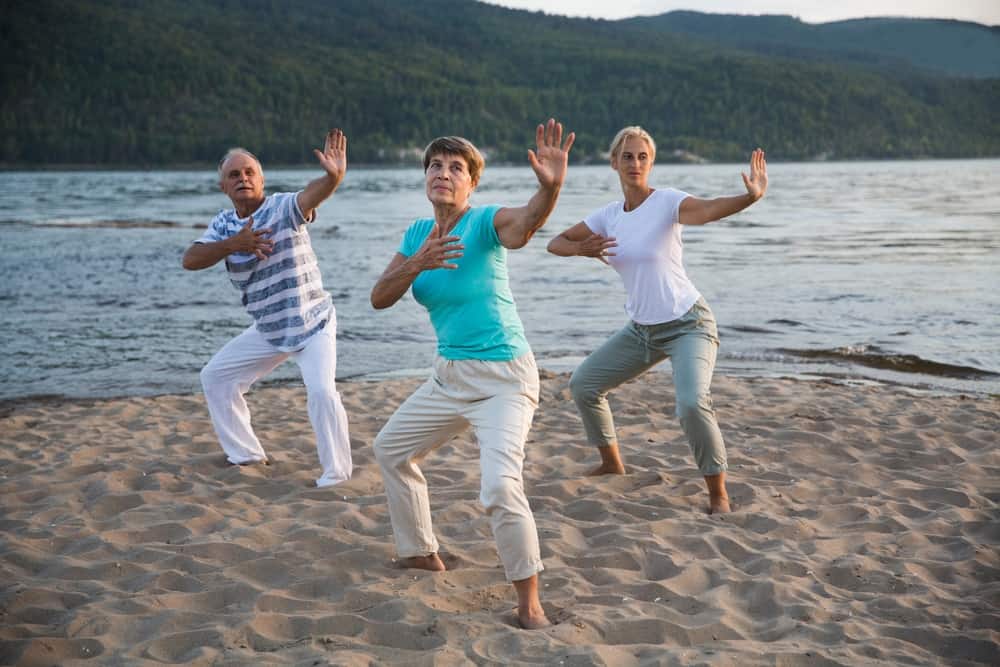 Three people on a beach practicing tai chi