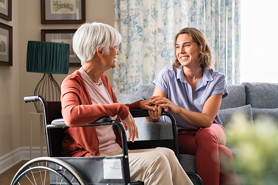 An adult child woman holds hands with a senior mother in a wheelchair