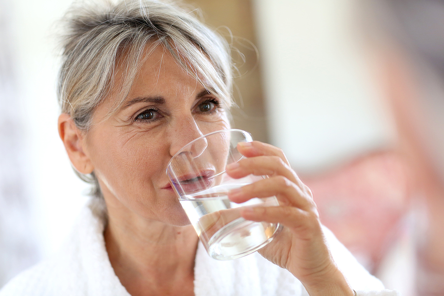 An older adult woman is drinking a glass of water in the morning